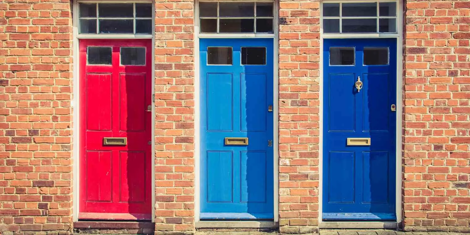 Three front doors in a brick terrace, painted red, light blue and dark blue